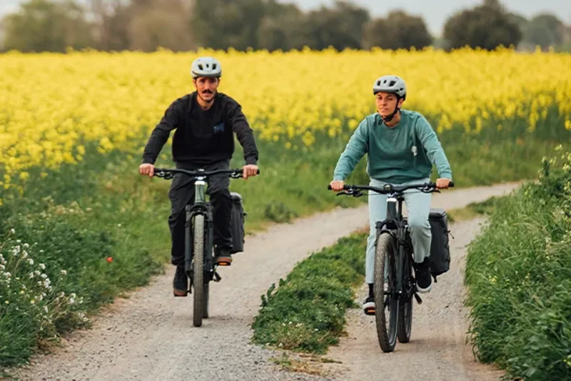 twoo riders on electric bikes cycling past a field of yellow flowers