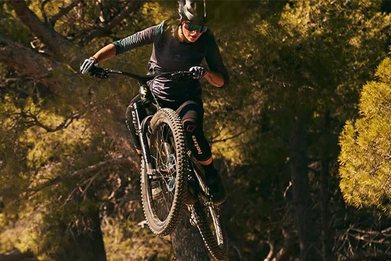 Woman riding an electric mountain bike over a jump in the woods