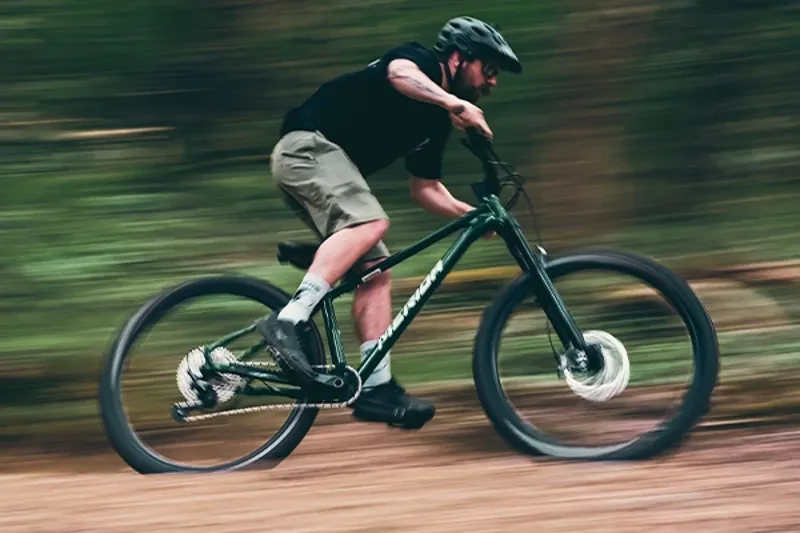 Woman riding a Merida hardtail mountain bike on singletrack in the woods on a sunny day