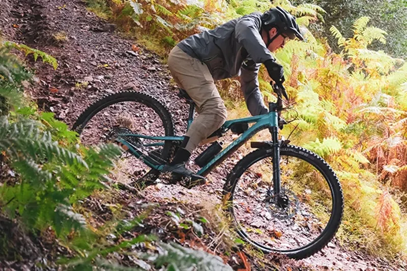Riding a Merida One-Twenty trail bike on dusty singletrack in the woods on a sunny day